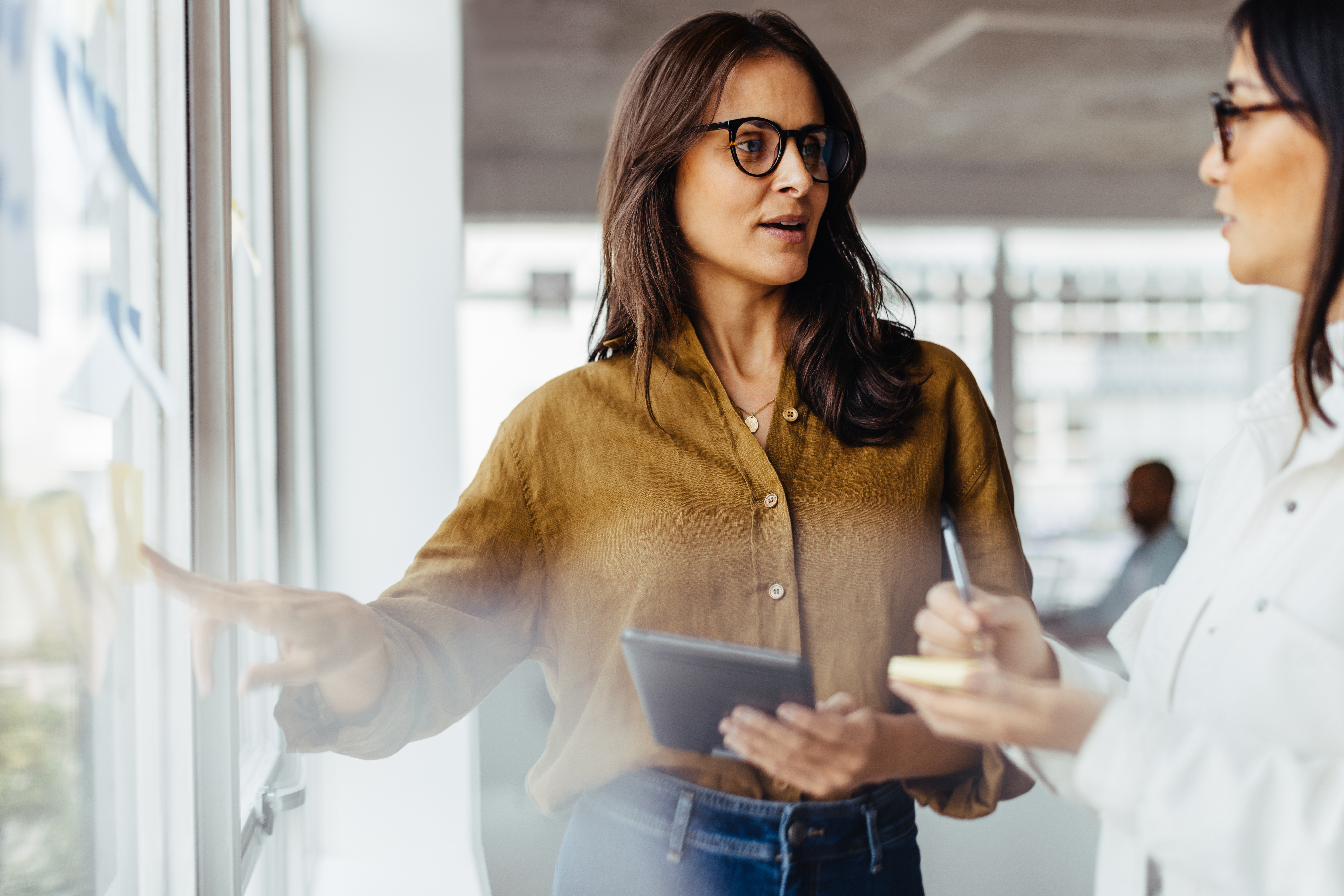 Business women discussing their ideas using sticky notes in an office. Female business professionals standing next to a window and brainstorming.