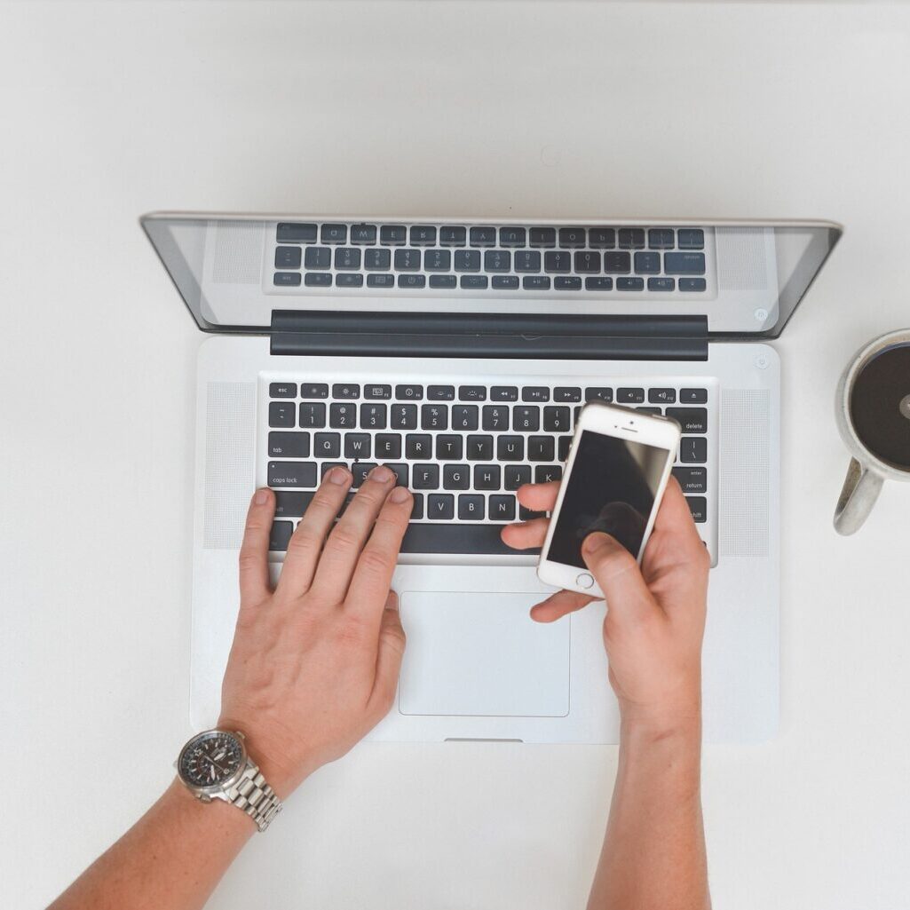 Mans-hands-at-a-laptop-holding-cell-phone-with-coffee-nearby Mans-hands-at-a-laptop-holding-cell-phone-with-coffee-nearby