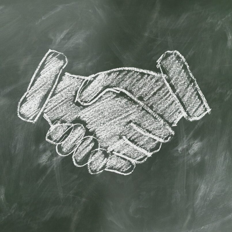 shaking hands drawn in white chalk on green board. shaking hands drawn in white chalk on green board.